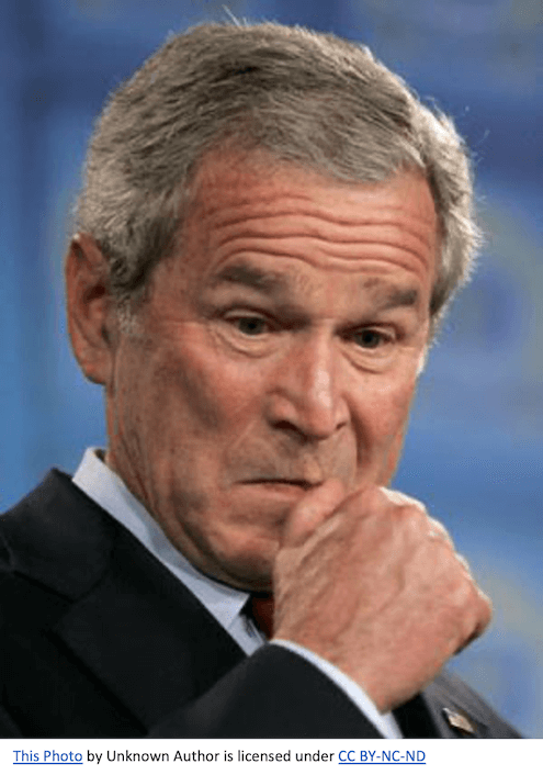 George W. Bush looking down, rubbing his thumb on his face.